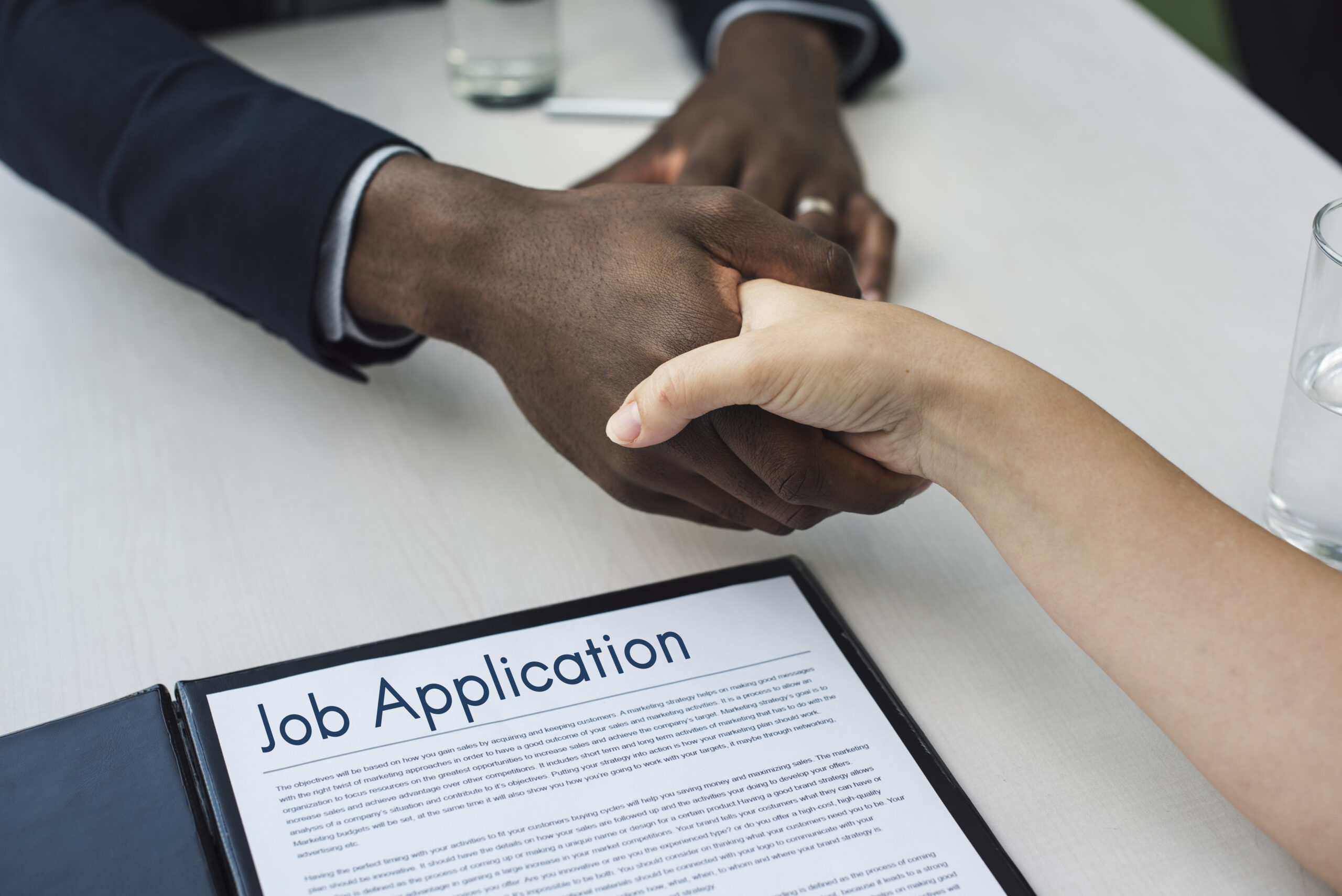 Close-up of two hands shaking over a "Job Application" document, symbolizing a fresh graduate beginning a career.