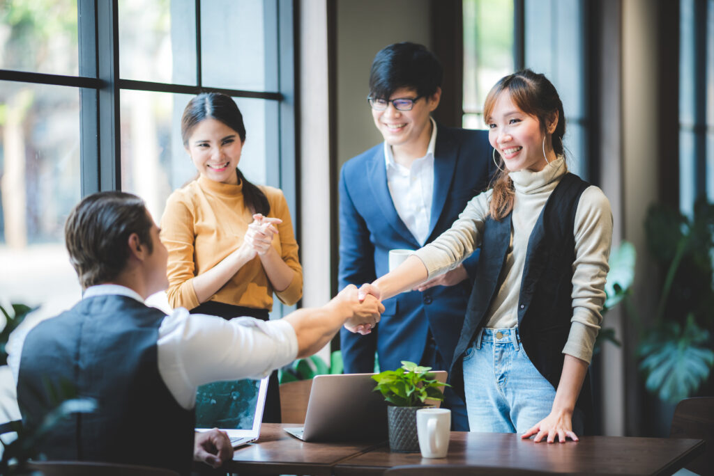 A woman with long brown hair shakes the hand of a man due to promotion to leadership role.